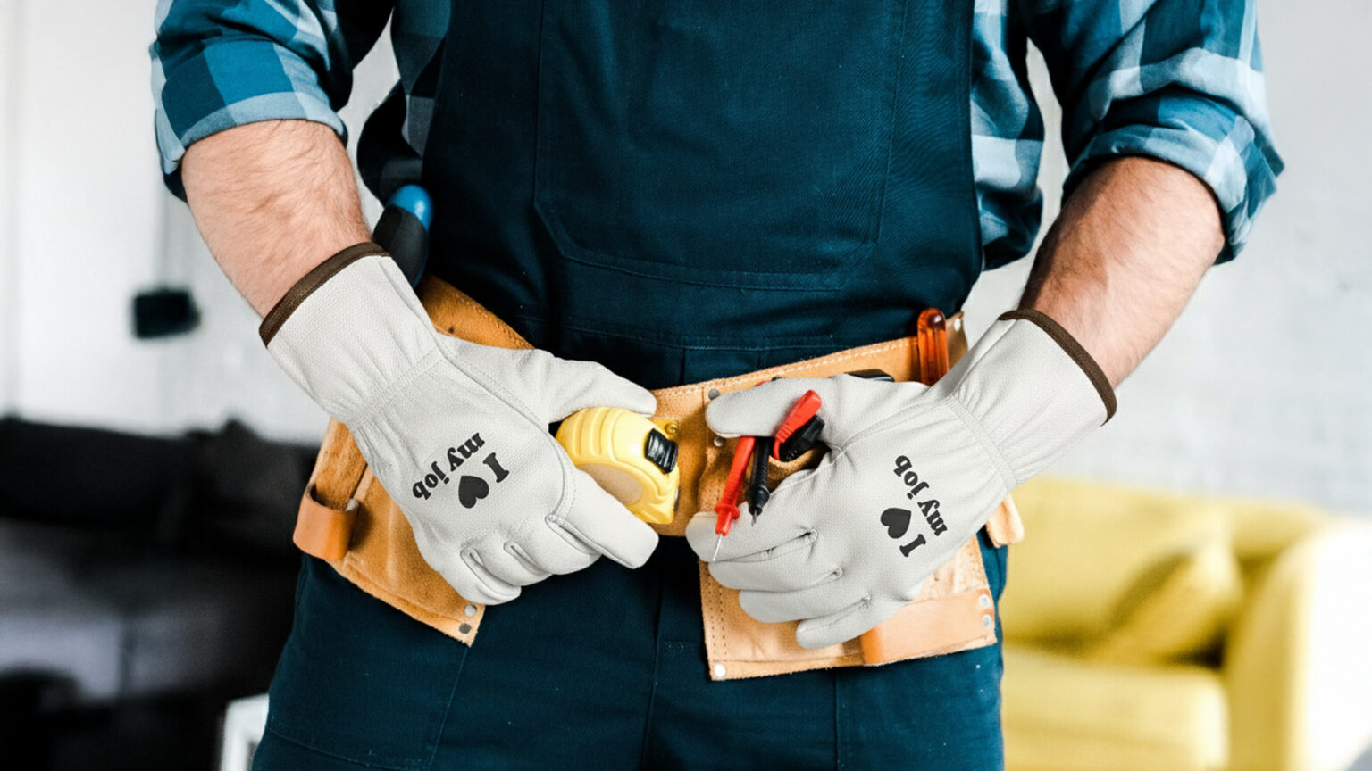 Mężczyzna w roboczym stroju trzyma narzędzia w skórzanym pasie, ma na dłoniach białe rękawice robocze z nadrukiem „I love my job”